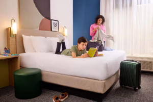 Focus: Peak of Summer Travels Kw: Best Affordable Hotels for Family Road Trips kid on hotel bed at Hilton Spark Affordable Family Summer Vacation Ideas