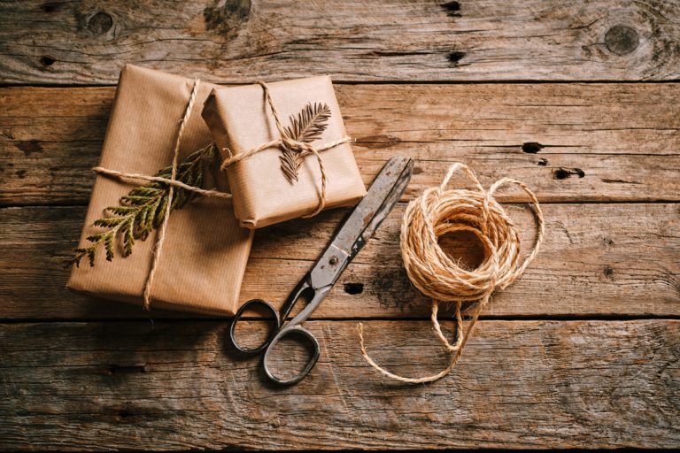 Two beautifully wrapped gifts with brown paper and twine are placed on a rustic wooden table. Scissors and natural decorations add charm to the scene. Outdoorsy Valentine's Day Gifts