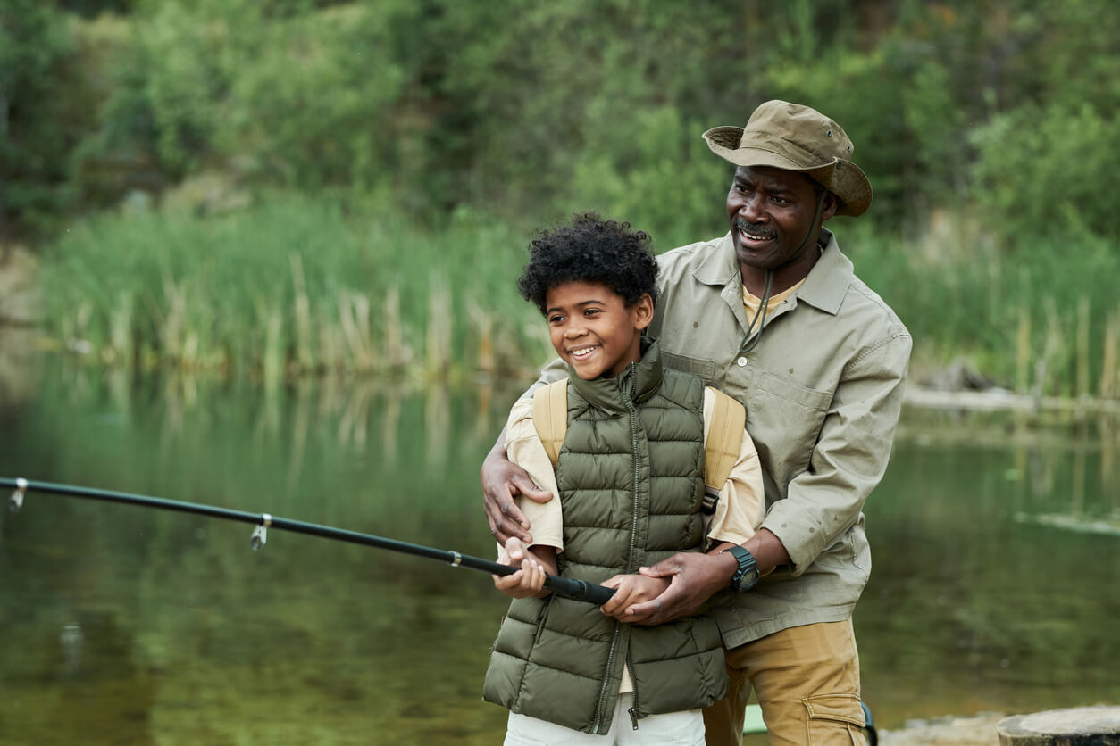 fishing with kids Happy African American dad catching fish together with his son on the lake outdoors