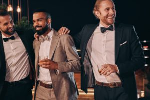 Three handsome men in suits bonding and drinking whiskey while spending time on party male wedding guest what to wear to a wedding