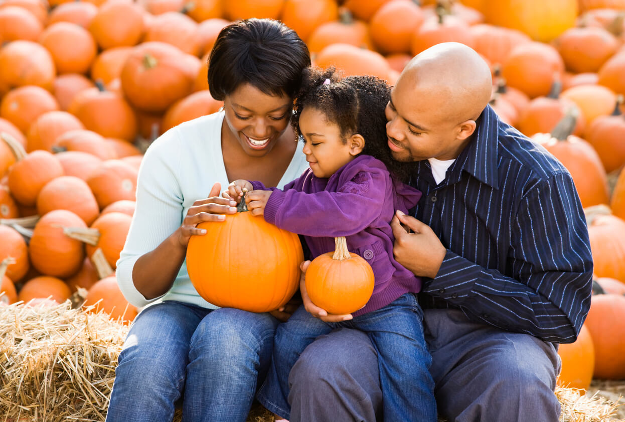 fall bucket list for families family at pumpkin patch for fall photos autumn Happy smiling family sitting on hay bales and holding pumpkins at outdoor market.