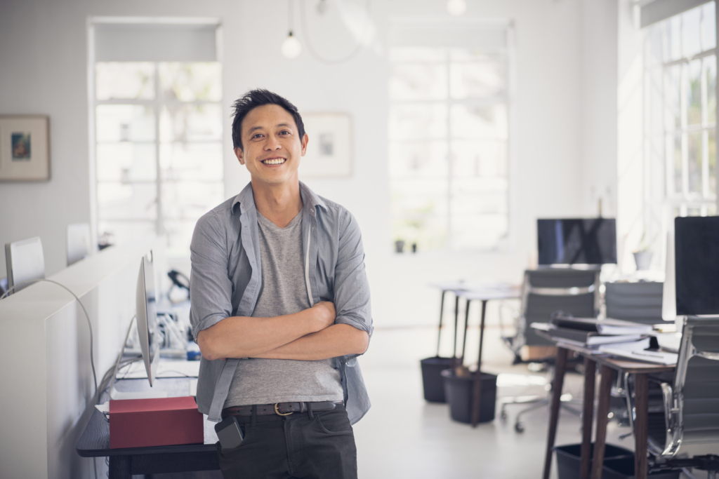 photo of happy businessman leaning on table. Portrait of expert with arms crossed. Smiling professional is in creative office.