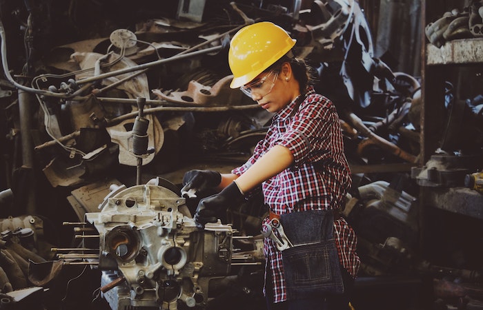 Woman Wears Yellow Hard Hat Holding Vehicle Part - is capital goods a good career path