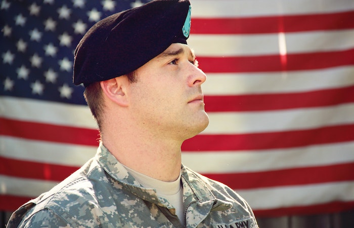 Man Wearing Combat Hat And Top Looking Up Near Flag Of America - hire military veterans