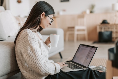 Content young businesswoman using laptop while taking tea cup at home - best jobs for weekends