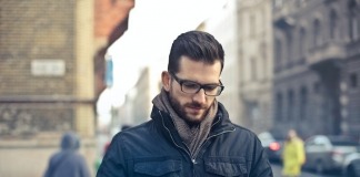 Man Wearing Black Zip Jacket Holding Smartphone Surrounded by Grey Concrete Buildings - best men's spring jackets