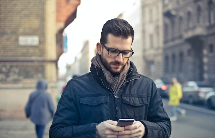 Man Wearing Black Zip Jacket Holding Smartphone Surrounded by Grey Concrete Buildings - best men's spring jackets